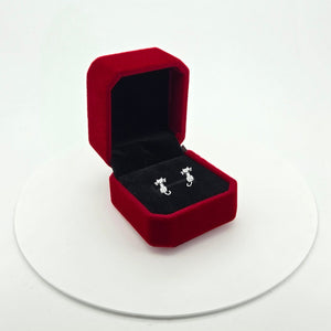 A pair of cat shaped sterling silver stud earrings displayed inside an open red velvet jewellery box on a white circular platform against a white background.