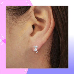 A close-up of a person's ear wearing a small sterling silver stud earring shaped like a cat with Cz stones, set against a pink and purple graphic border.