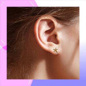 A close-up of a person's ear wearing a small gold starfish stud earring, framed by a pink and purple graphic border.
