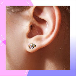 A close-up of a person's ear wearing a small colorful clownfish stud earring, with a pink and purple graphic border around the photo.