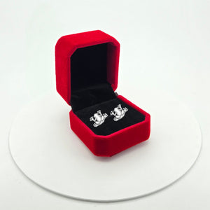 A pair of silver frog stud earrings displayed inside an open red velvet jewelry box on a white circular platform against a white background.