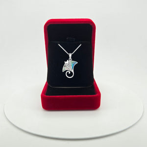 A silver pendant necklace featuring a stylized manta ray design with iridescent abalone shell inlay displayed inside an open red velvet jewellery box on a white circular platform.