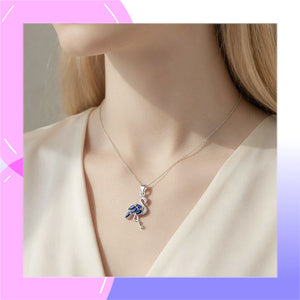 A silver-toned flamingo pendant necklace with blue and white enamel detailing, shown worn on a model's neck against a soft cream blouse.